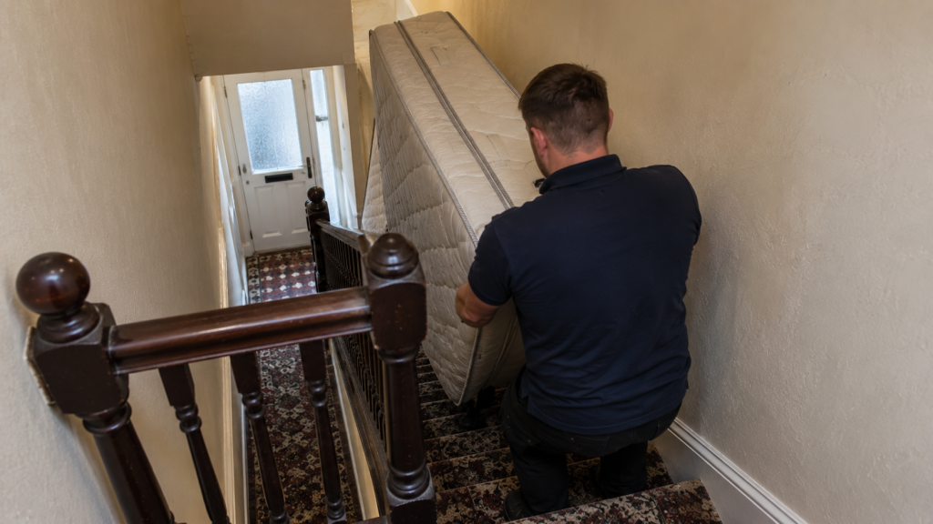 Worker carrying a mattress down a narrow staircase